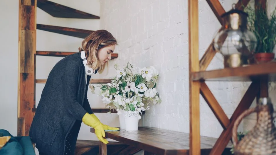 a-woman-in-a-green-shirt-and-black-gloves-vacuuming-a-gray-ottoman-5txz228u4eo